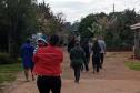 Imagem mostra um grupo de pessoas caminhando por rua de barro. No primeiro plano uma mulher carrega um bebê. 