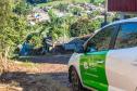 Imagem mostra carro da DPE-PR em rua calçada com pedras e ao fundo casas em meio à plantações. 