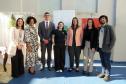 Um grupo de sete pessoas posa para uma foto. São defensores e assessores da DPE-PR. Eles estão no pátio da prisão, em frente banners da Defensoria e do Conselho da Comunidade. As vestimentas são formais e a atmosfera é de satisfação e dever cumprido.