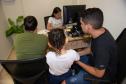 Casal acompanhando por uma menina, todos de costas, são atendidos por uma servidora da DPE-PR em Mutirão Concilia.   