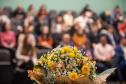 Em primeiro plano flores e ao fundo auditório lotado com familiares dos novos servidores.
