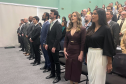 Novos defensores públicos e o público presente no auditório da Defensoria acompanham o hino nacional durante a solenidade de posse. 