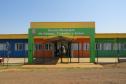 A foto mostra a fachada colorida de uma escola rural, com paredes pintadas em azul, laranja e verde. Um grande portal verde sobre a entrada tem a inscrição "Escola Municipal do Campo, Trabalho e Saber". O dia está ensolarado, com céu azul e sem nuvens.