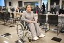 Uma mulher sentada em cadeira de rodas posa para foto durante o Mutirão de Saúde da Defensoria na Camara Municipal de Curitiba.  
