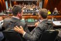 Defensores públicos de costas se cumprimentam na mesa diretora do lançamento do NUPED. Ao fundo o público presente. 