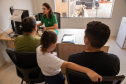 Imagem mostra uma família com pai, mãe e filha - todos de costas - numa sala recebendo atendimento de uma defensora pública. 