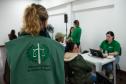 Imagem mostra equipe da Defensoria Pública realizando atendimentos em Mutirão. No primeiro plano se vê uma mulher de costas com o colete da Defensoria e ao fundo a equipe e e usuários desfocados. 