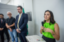 Em um plano mais aproximado, a mulher de blusa verde discursa ao microfone com expressão atenta, apoiada em um púlpito com papéis. Logo atrás dela, três homens aguardam em pé, escutando-a com seriedade.