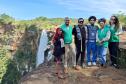 Equipe da Defensoria posa ao lado de indígenas e ao fundo uma cachoeira que fica dentro do território. 