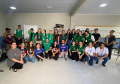 Fotografia de um grande grupo posando sorridente em um salão claro. Muitas pessoas vestem o colete verde da DPE-PR, acompanhadas por outras em trajes casuais. Ao fundo, há letreiros indicando "Centro POP".