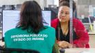 Imagem mostra servidor de costas com colete verde onde se lê Defensoria Pública do Parané e ao fundo uma mulher assistida durante Mutirão Meu Pai Tem Nome. 