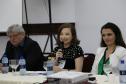 Vemos três pessoas sentadas em uma mesa. Gabriele Rezende, no meio segurando um microfone perto de sua boca, o Ouvidor-Geral a sua direita e a Diretora da EDEPAR a sua esquerda. 