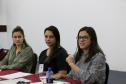 Temos as Assistentes Sociais do CAM Ponta Grossa, Ana Letícia de França e Evelyn Soares,ao fundo, sentadas no lado direito da mesa de falantes e  Taísa de Oliveira ,Assistente Social do CAM Curitiba, na ponta esquerda da mesa. 