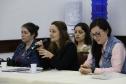 Vemos três participantes do evento. Camylla Basso, sentada centralmente, psicologa da Coordenação de Planejamento aparenta estar realizando uma pergunta.  