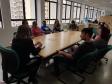 Mesa da reunião, os representantes estão sentados em volta da mesa. De costas, no início da foto, está presente a dra. Olenka Lins.