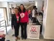 As duas palestrantes encontram-se juntas, no CAM Curitiba, após o termino da palestra. Ambas estão sorrindo para a foto e há um cartaz da Associação Amigas da Mama ao seu lado. 