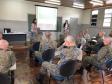A foto foi tirada no fundo da sala. Nela vemos os soldados sentados em algumas certeiras prestando atenção na equipe da DPPR que está na parte da frente da sala, palestrando, 