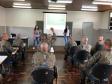 A imagem foi tirada novamente no fundo da sala. Vemos os soldados sentados nas carteiras e a equipe da DPPR na frente. Nessa imagem vemos que um dos alunos está com a mão levantada. 