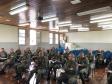 A imagem foi tirada na parte da frente focando nos alunos. Vemos esses prestando atenção na equipe da DPPR que está fora do quadro da imagem. 