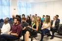 Na imagem vemos o público do evento, estão todos sentados, prestando atenção em algo que lhes é dito/mostrado a sua frente. 