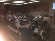 Imagem tirada durante uma palestra. Mostra uma palestrante de frente para o público. 
