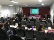 Imagem tirada durante a palestra do funda da sala. Vemos as costas dos ouvintes e a palestrante a frente. 