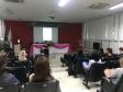 Imagem também tirada durante a palestra do funda da sala. Vemos as costas dos ouvintes e a palestrante a frente. 