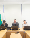 Imagem do defensor público-geral no centro mexendo no computador, ao lado direito está o defensor público Nicholas e ao esquerdo o defensor público Pedro. No fundo, está uma cortina branca e a bandeira do brasil e da Defensoria no lado esquerdo. 