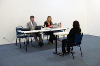 Imagem da banca com dois defensores, um homem e uma mulher, sentados enquanto conversam com uma candidata que está sentada na sua frente.