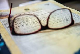 Imagem mostra uma imagem de um óculos sobre um documento desfocado. 