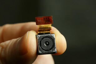 Imagem de uma micro camera em close entre os dedos. 