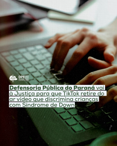 Imagem desfocada de um computador com o título "Defensoria Pública do Paraná vai à Justiça para que Tik Tok retire do ar vídeo que discrimina crianças com Síndrome de Down", tarjado em branco. Acima o logo da Defensoria em branco.