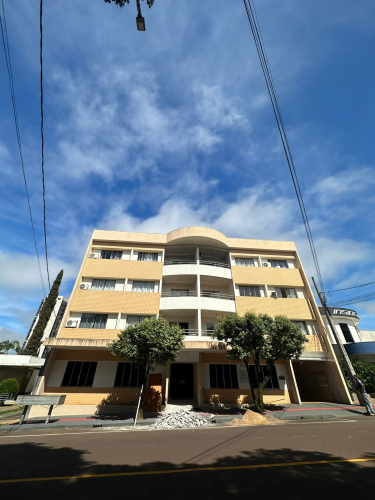 Imagem que mostra a fachada do prédio onde vai funcionar a sede da Defensoria em Campo Mourão. Trata-se de um prédio baixo, com térreo e 3 andares. Em frente ao prédio há duas árvores baixas e, na rua, ao lado da calçada, há dois montes de areia e entulho que indicam que o local está em obras. Acima do prédio é possível ver o céu, bem azul e com algumas nuvens.
