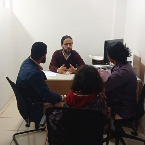 Imagem do defensor Fernando atendendo um homem, uma mulher com bebê de colo uma criança, em uma sala.