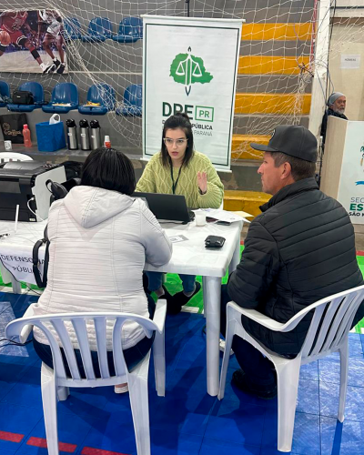 Imagem de uma servidora realizando atendimento a duas pessoas.