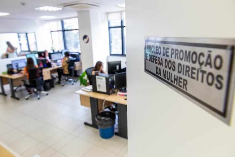 Imagem mostra placa do Nudem na porta e ao fundo equipe atuando.