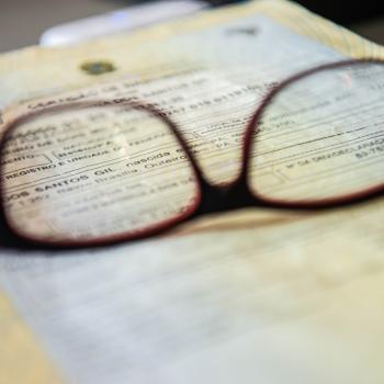 Imagem mostra uma imagem de um óculos sobre um documento desfocado. 