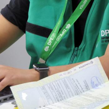Imagem mostra detalhe de servidora com colete da DPE-PR. 
