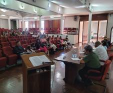 Imagem que mostra a mesma mesa de abertura do evento e também a plateia, formada por diversas servidoras e servidores da Defensoria.