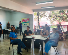 Imagem que mostra diversas pessoas aguardando atendimento no mutirão de Cascavel. Algumas pessoas estão em pé, outras estão sentadas em cadeiras, ao redor de mesas, na faculdade Unipar, onde foi realizado o evento.