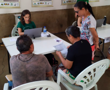 Imagem que mostra um atendimento no mutirão. Três pessoas estão sendo atendidas por uma mulher, a defensora pública Aline Bastos, que está olhando para um notebook. Duas pessoas que estão sendo atendidas analisam um documento.
