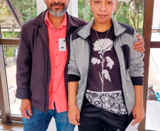 Imagem que mostra a usuária da DPE-PR Priscila Patrícia Rodrigues ao lado do pai. Eles estão de pé e o pai está com uma das mãos no ombro da filha.