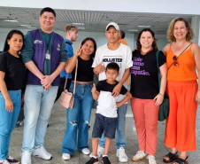 Imagem da família mencionada na matéria, a foto conta com a família acompanhada da equipe que auxiliou o reencontro, eles estão posando para a foto no aeroporto.