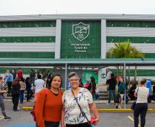 Imagem que mostra as candidatas Stela Maris Dabul e Roselaine Gomes dos Santos em frente ao local de prova, um dos prédios da Universidade Tuiuti, em Curitiba. Stela Maris usa uma blusa estampada e Roselaine, uma blusa de mangas compridas laranja. As duas olham para a frente.