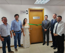 Imagem que mostra a inauguração da sala da DPE-PR no Fórum de Cambé, onde estão o prefeito de Cambé, o deputado estadual Tiago Amaral, a defensora pública Aline Bastos, o defensor-geral do Paraná, o juiz Ricardo Gorla e o representante da OAB David Garcia. Todos estão ao lado da porta da sala da Defensoria e sorriem.