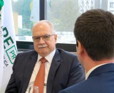 Imagem do Ministro Fachin sentado à mesa e olhando para o defensor público Matheus Munhoz, com quem estáva conversando no momento.