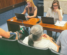 Imagem de uma foto de um atendimento presencial, duas servidoras públicas estão conferindo informações em seus notebooks enquanto três usuários da Defensoria Pública aguardam. Na parte central inferior da imagem, está o título da matéria.
