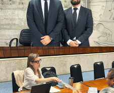 Imagem em formato de colagem entre duas fotos, a primeira, na parte de cima, mostra dois defensores posando para uma foto, um deles é o Rafael de Matos Souto e ao seu lado, Bruno de Almeida Passadore. Na foto de baixo, mostra uma servidora pública estendendo uma folha para um dos usuários da Defensoria Pública.