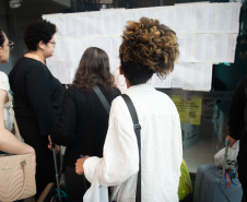 Imagem horizontal colorida que mostra os candidatos conferindo seus locais de provas no mural.