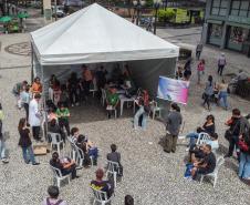 Imagem horizontal colorida feita de drone em que aparece a tenda montada na Boca Maldita e as pessoas aguardando o atendimento para o Mutirão da DPE-PR.